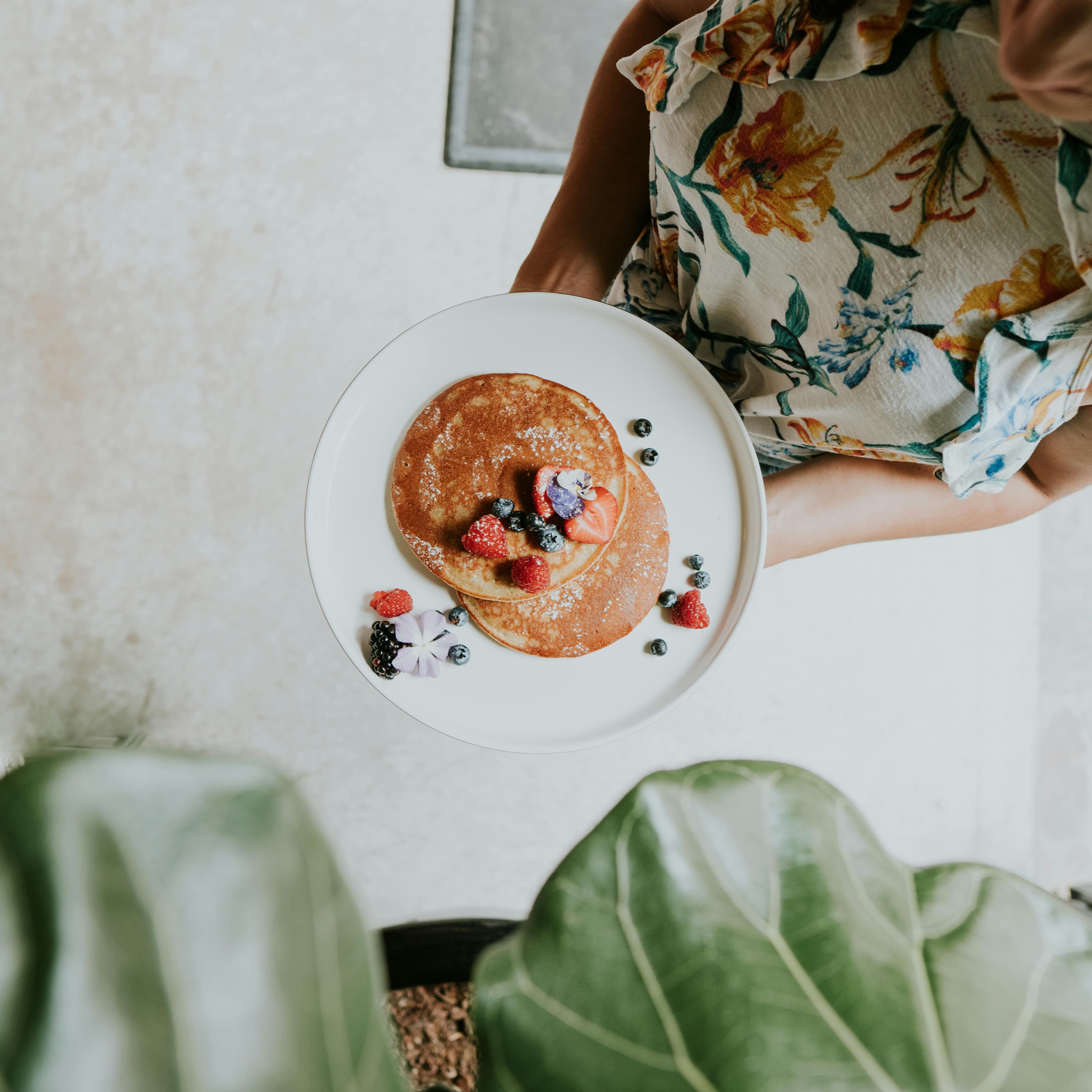 Overhead view of a woman holding a plate with pancakes topped with assorted fresh berries.