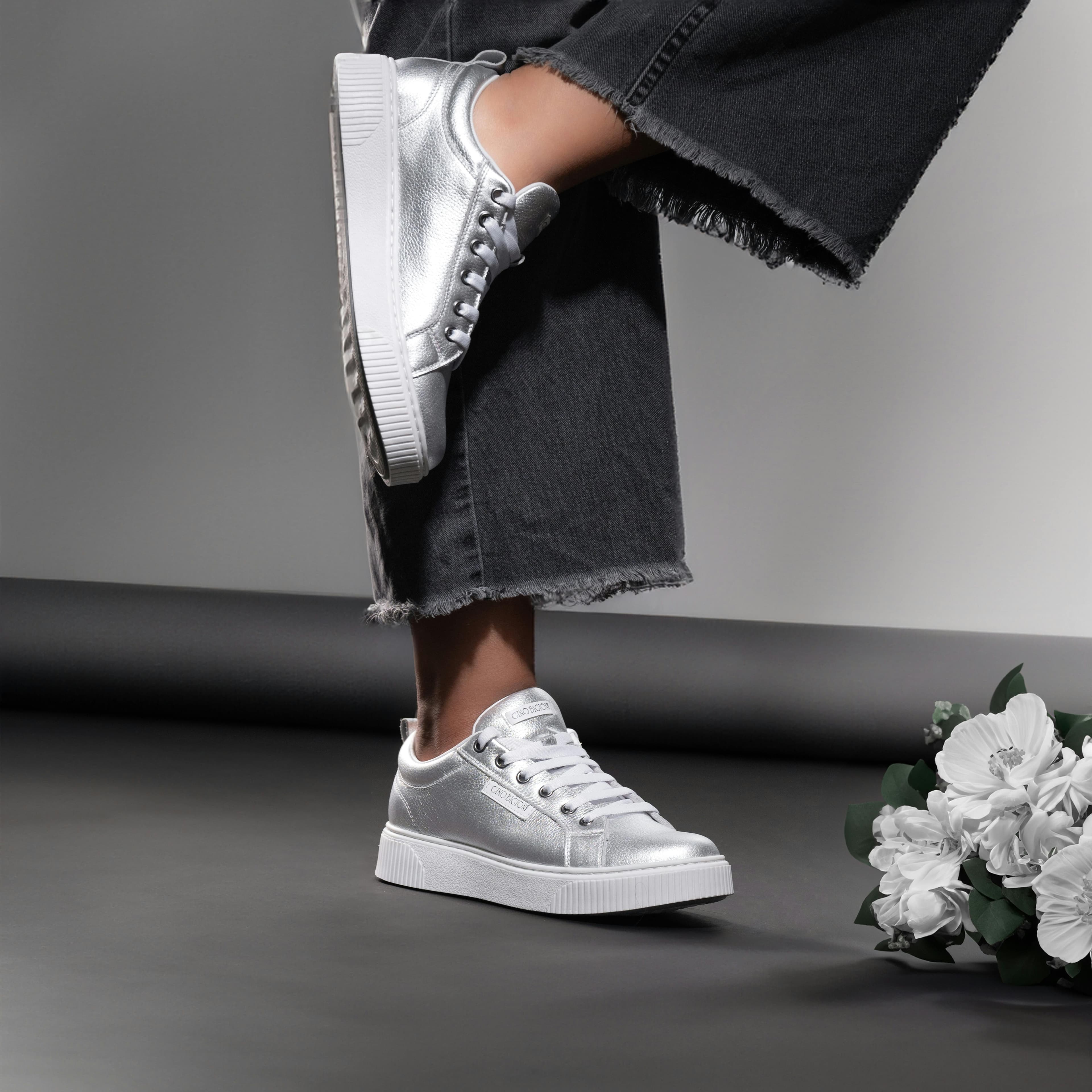 Featuring a woman in trendy silver sneakers against an elegant grey backdrop.