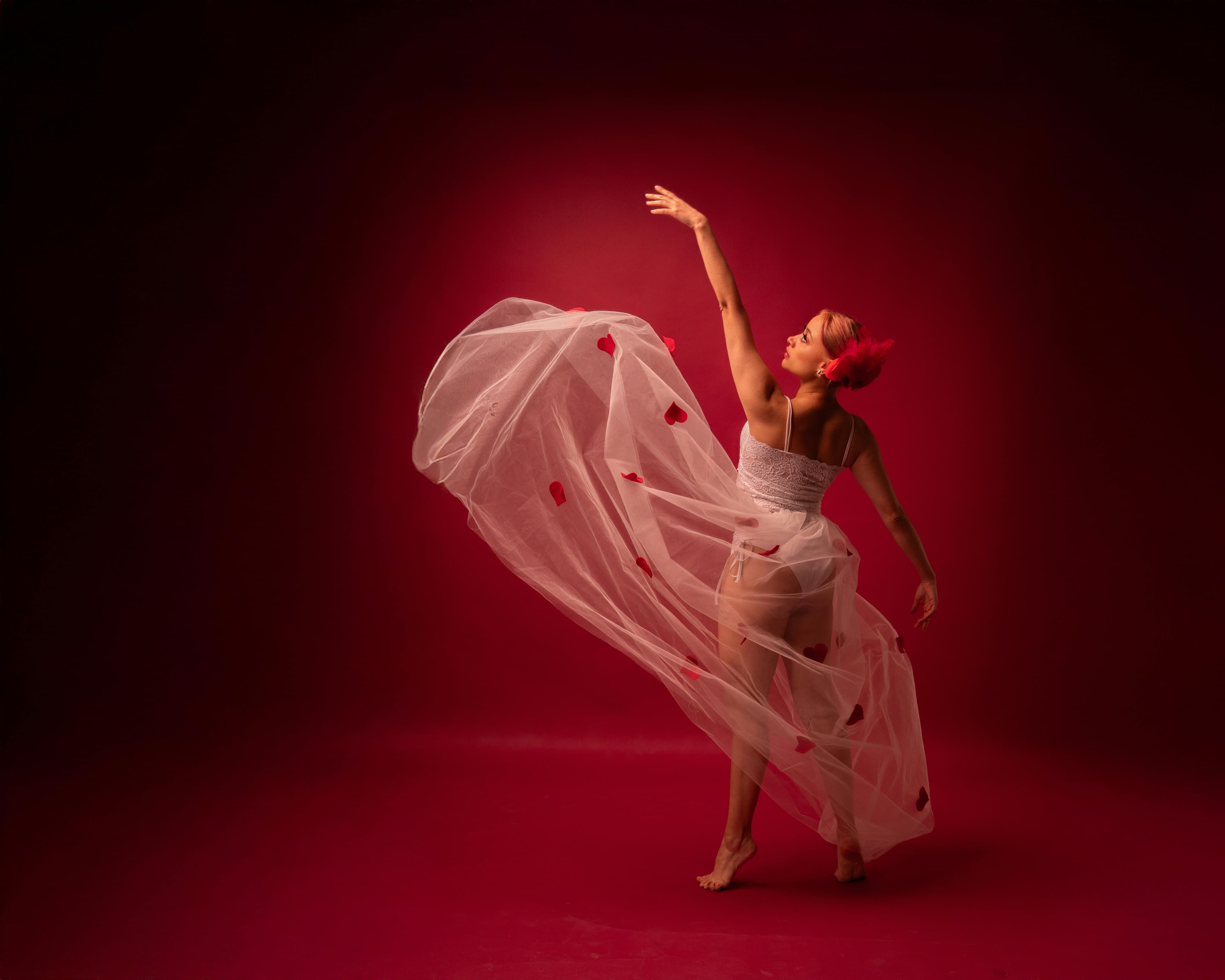 Elegante bailarina contemporánea con un vestido fluido con corazones rojos, sobre un fondo rojo intenso.