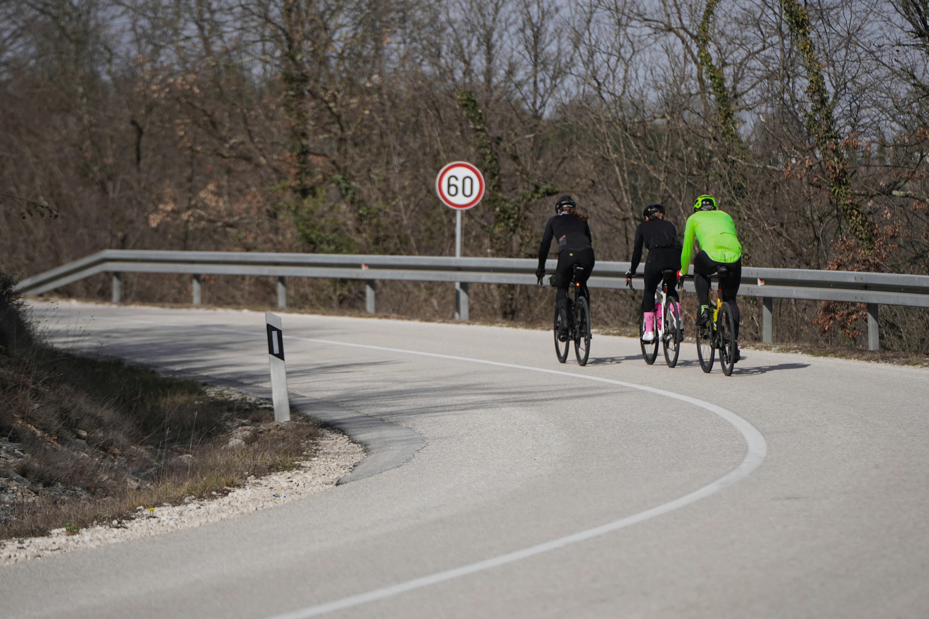 Drei Radfahrer fahren eine kurvenreiche Straße in Kroatien bergauf, aufgenommen bei Tageslicht.