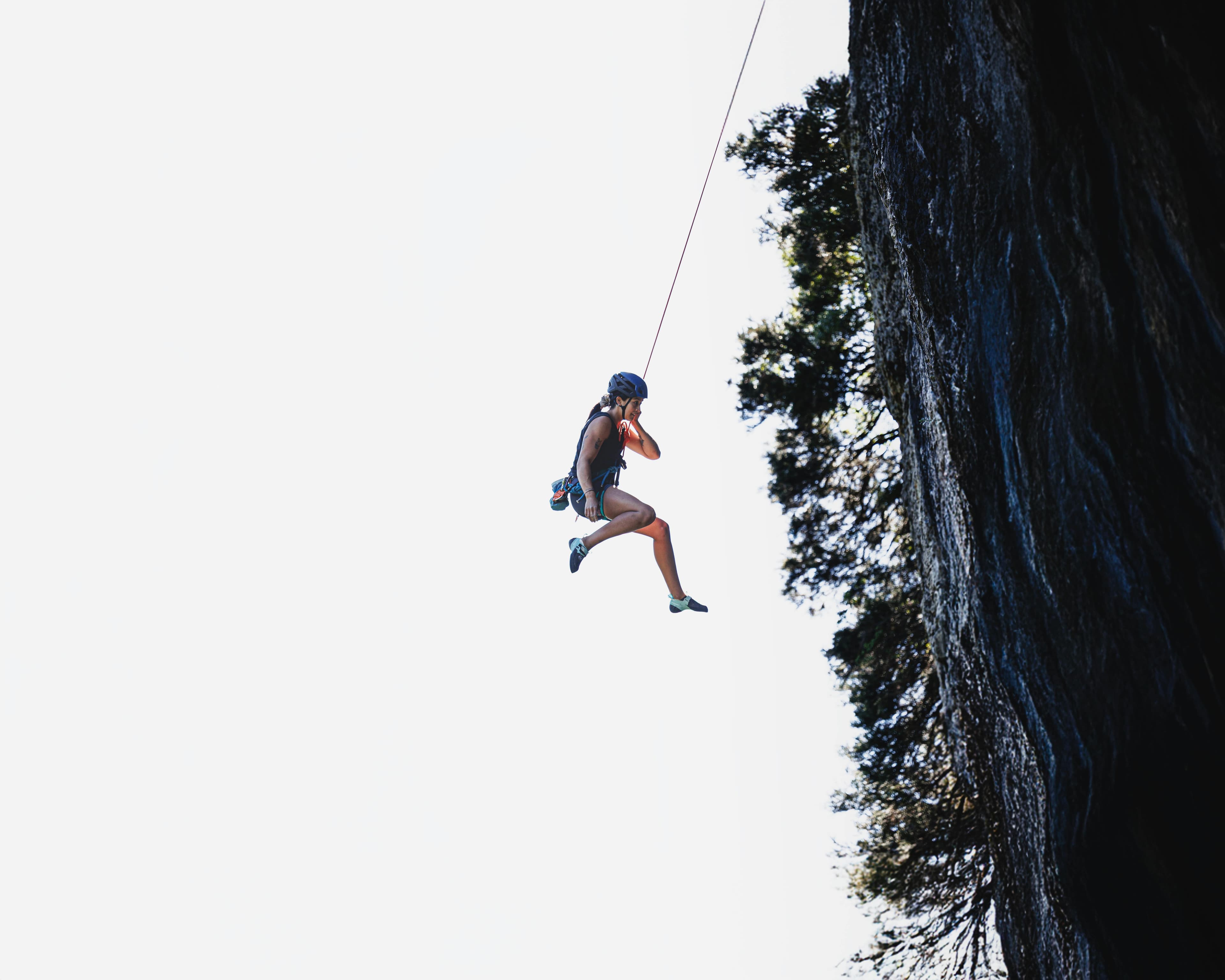 Une femme descend en rappel le long d'une falaise avec un équipement de sécurité par temps clair. Aventure et exploration.