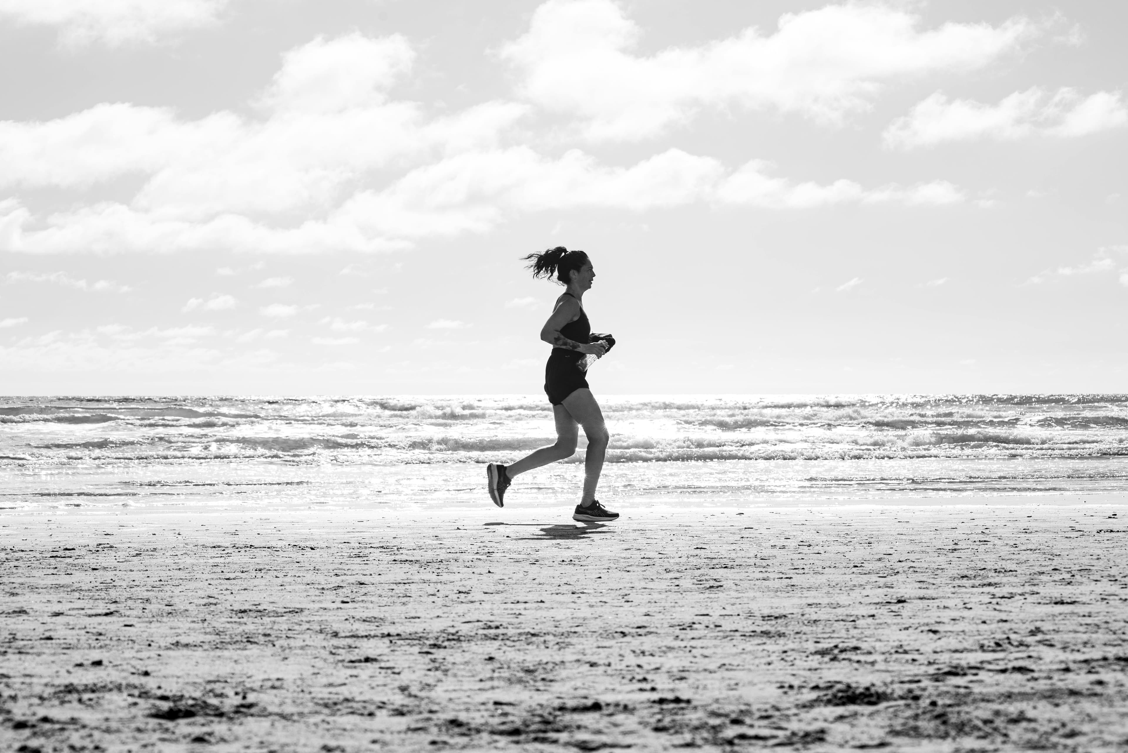 Eine Frau joggt am Strand von La Lucila del Mar in Argentinien in einer monochromen Umgebung. Fitness und Freiheit einfangen.