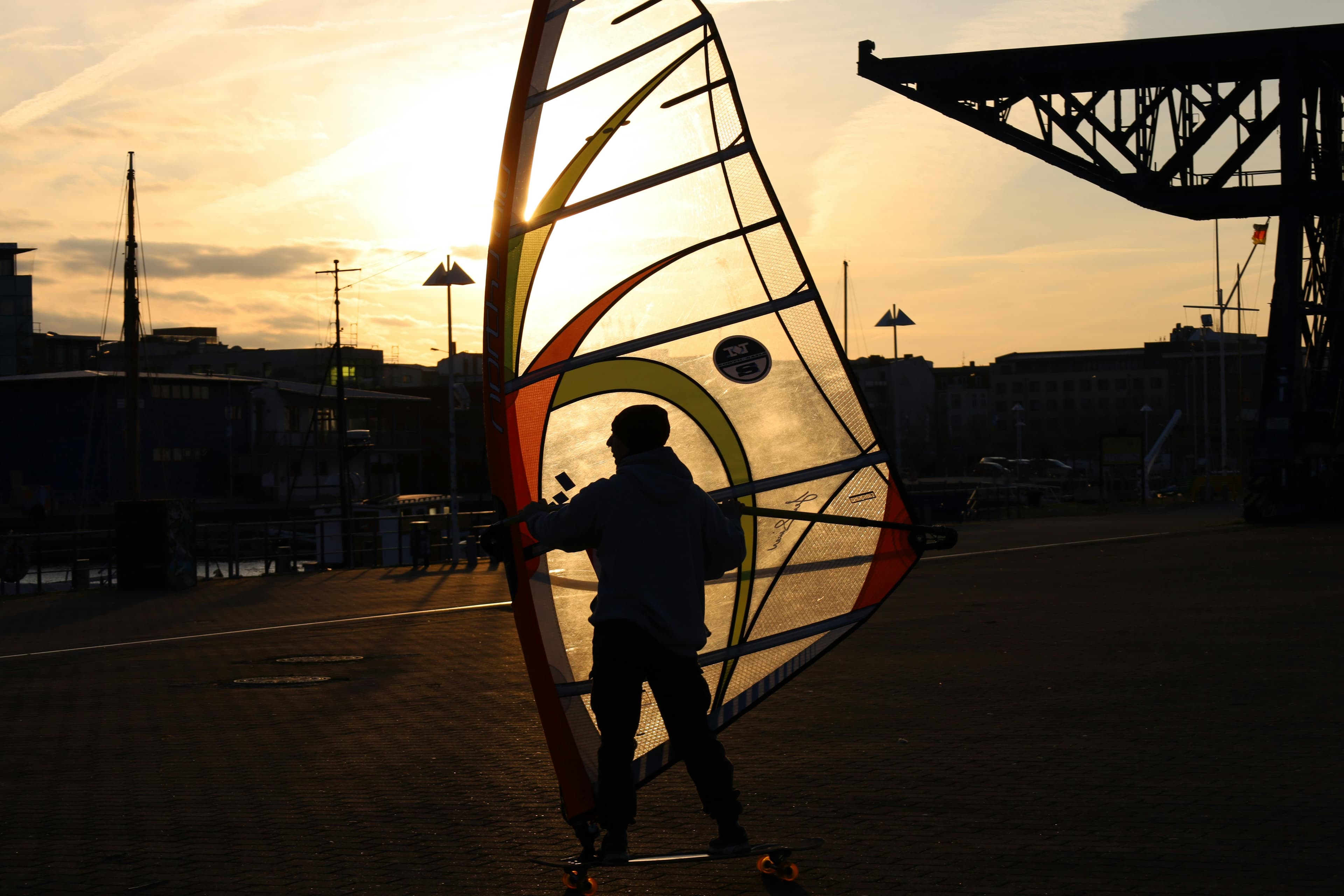 Silhuet af en windsurfer i Rostock byhavn under en livlig orange solnedgang, Tyskland.