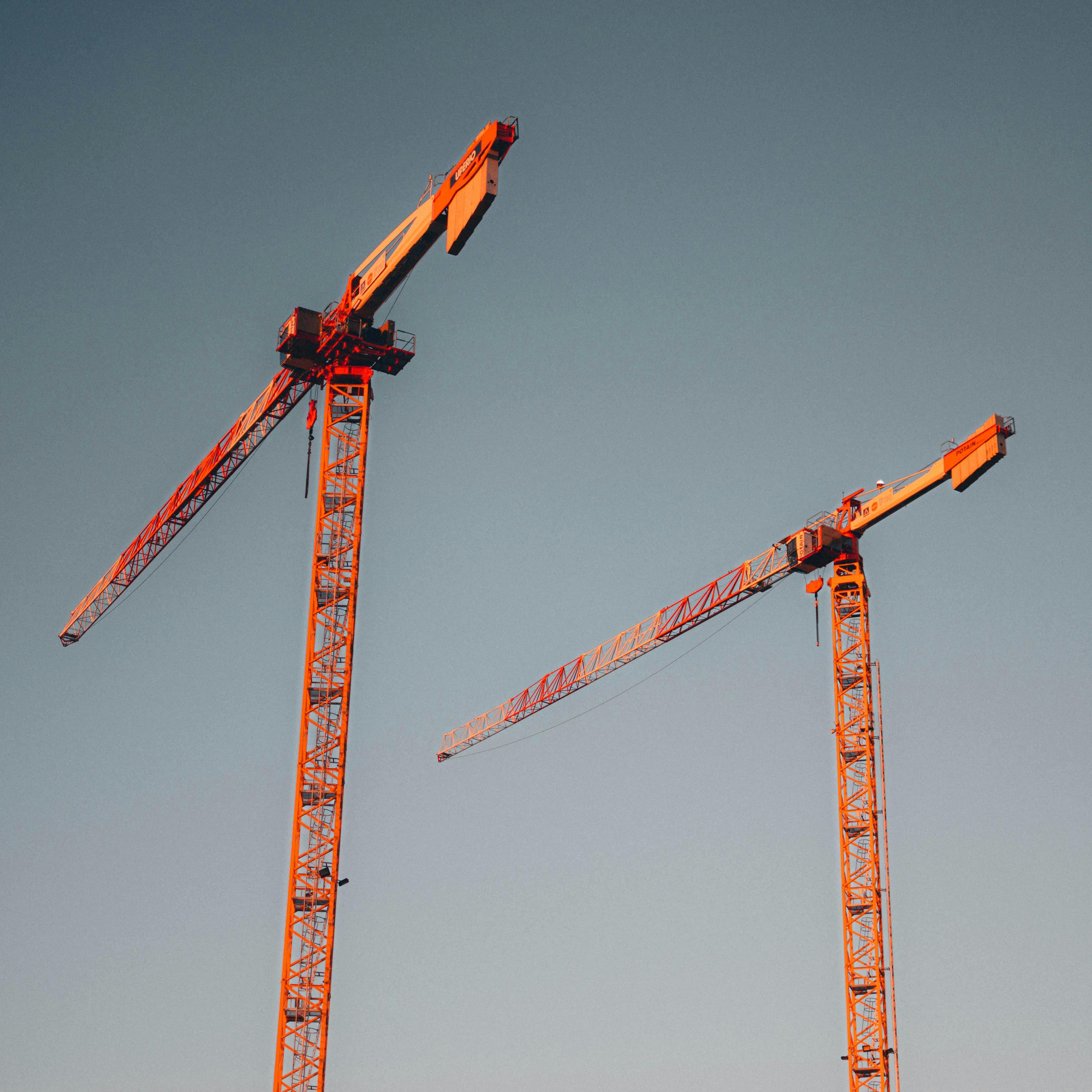 Dos grúas torre rojas se alzan contra un cielo despejado, simbolizando el desarrollo urbano.