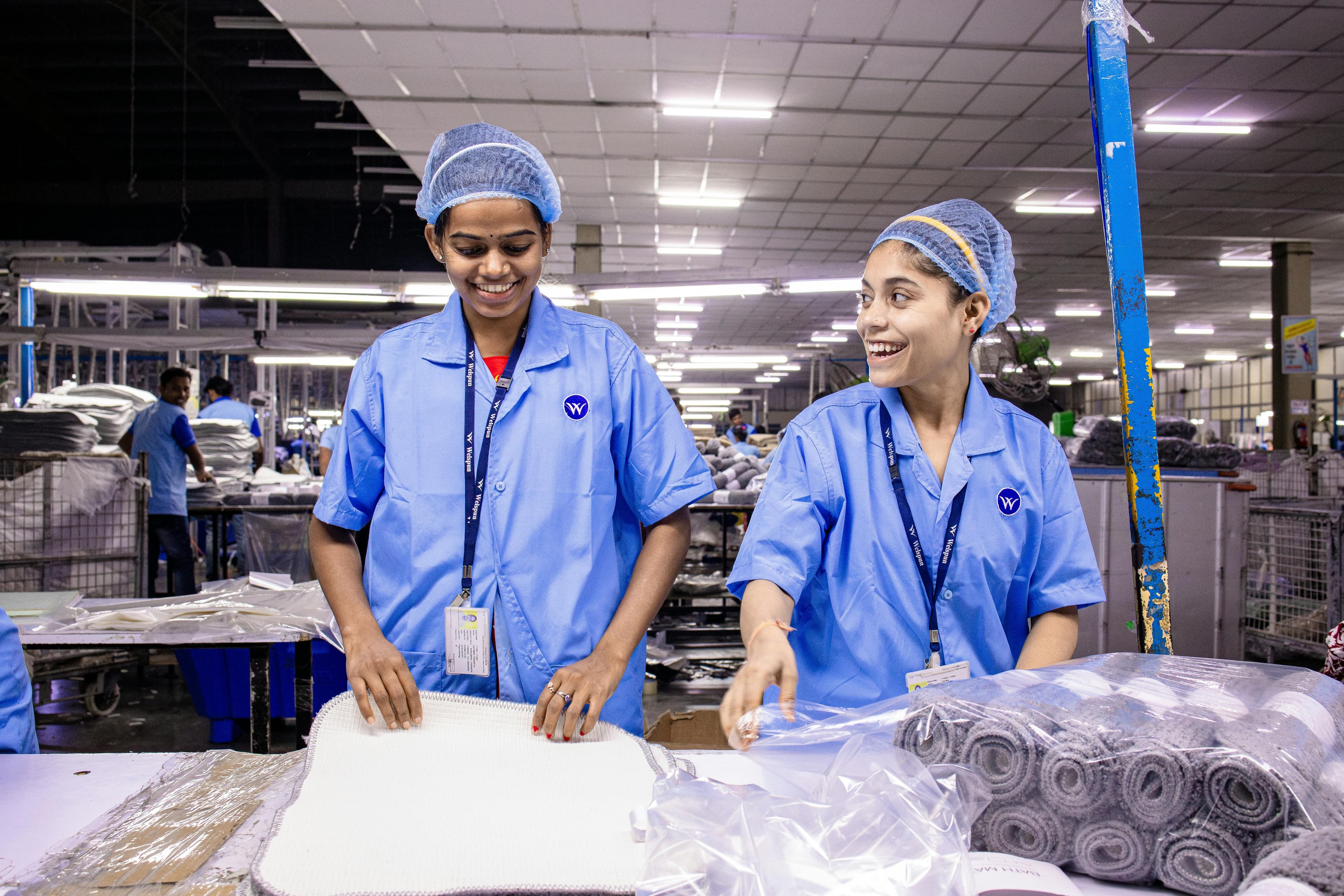 Magazzinieri tessili in divisa blu che imballano i materiali sorridendo.