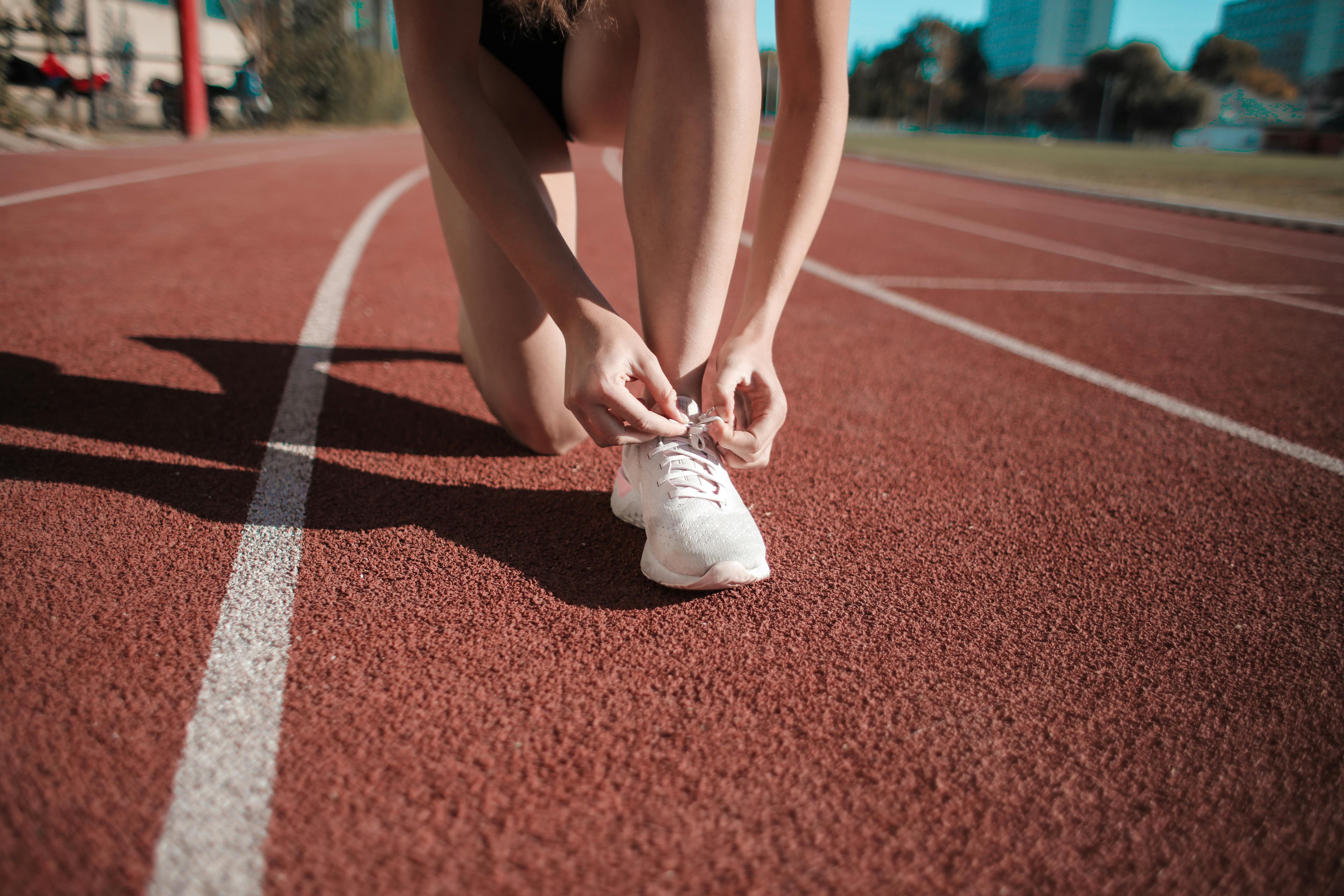 Close-up of a woman tying her shoes on a running track, ready to sprint.