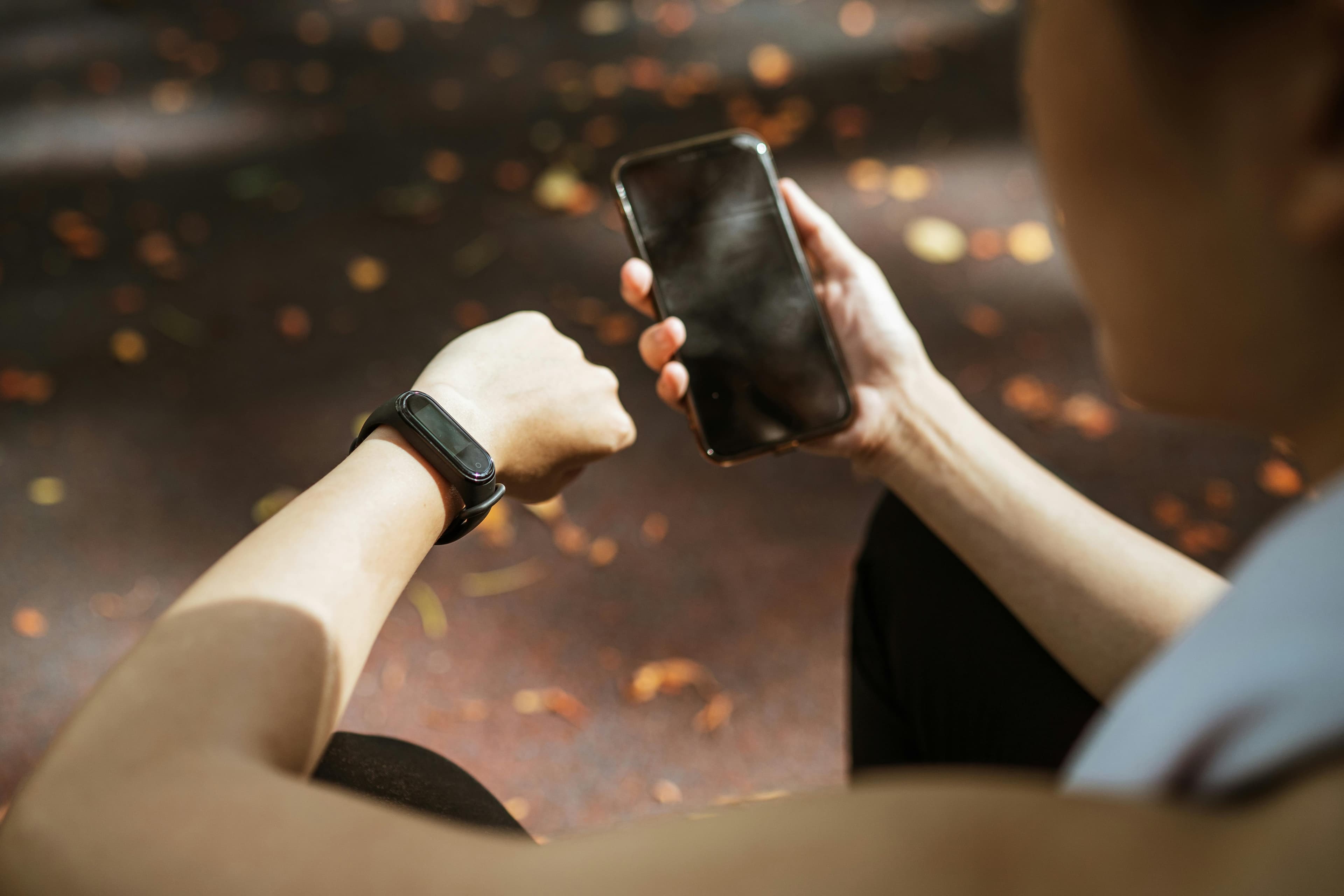 Back view of anonymous female using smartphone app and smart watch after jogging in park