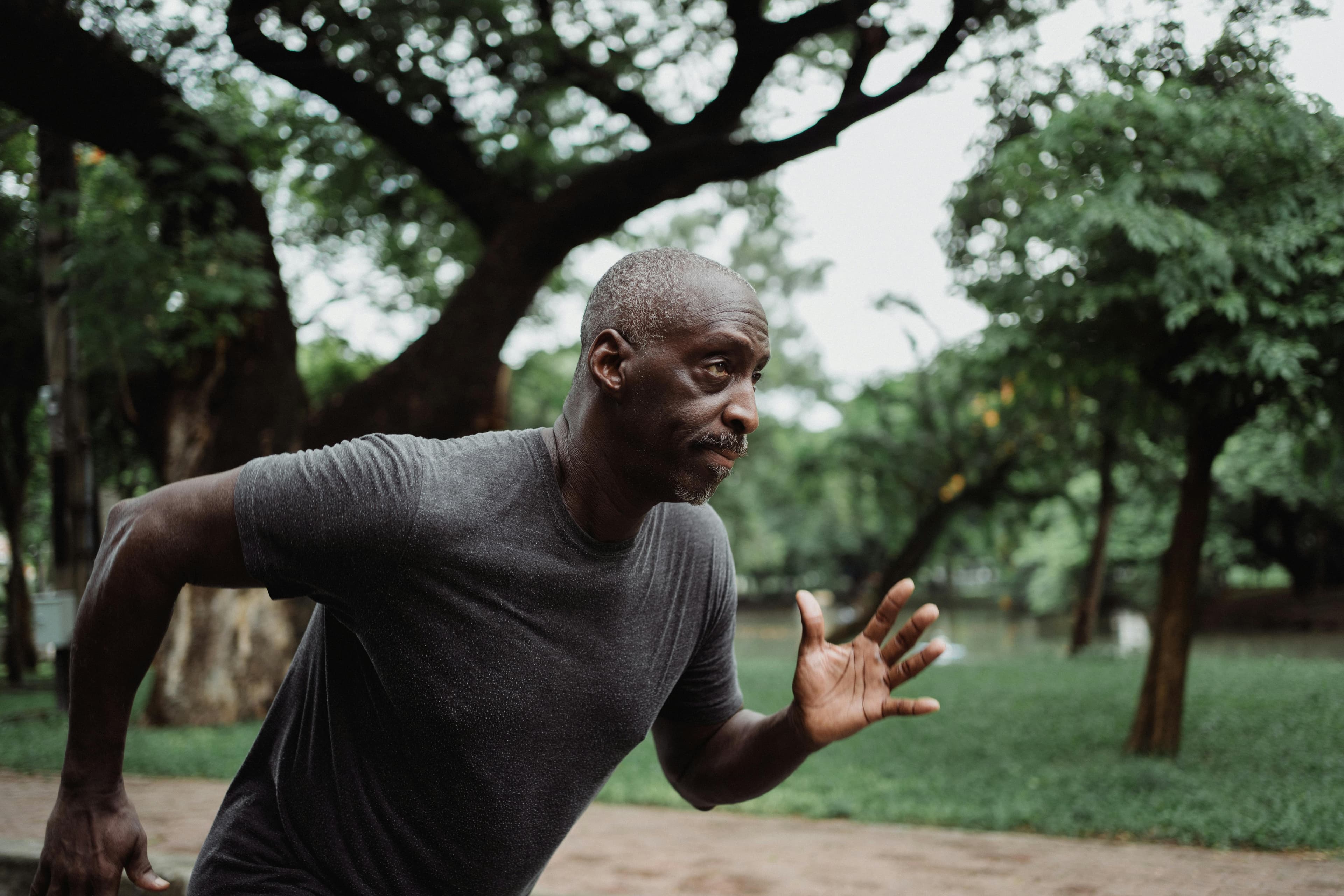 Focused black male adult running energetically in a green park, promoting fitness and health.