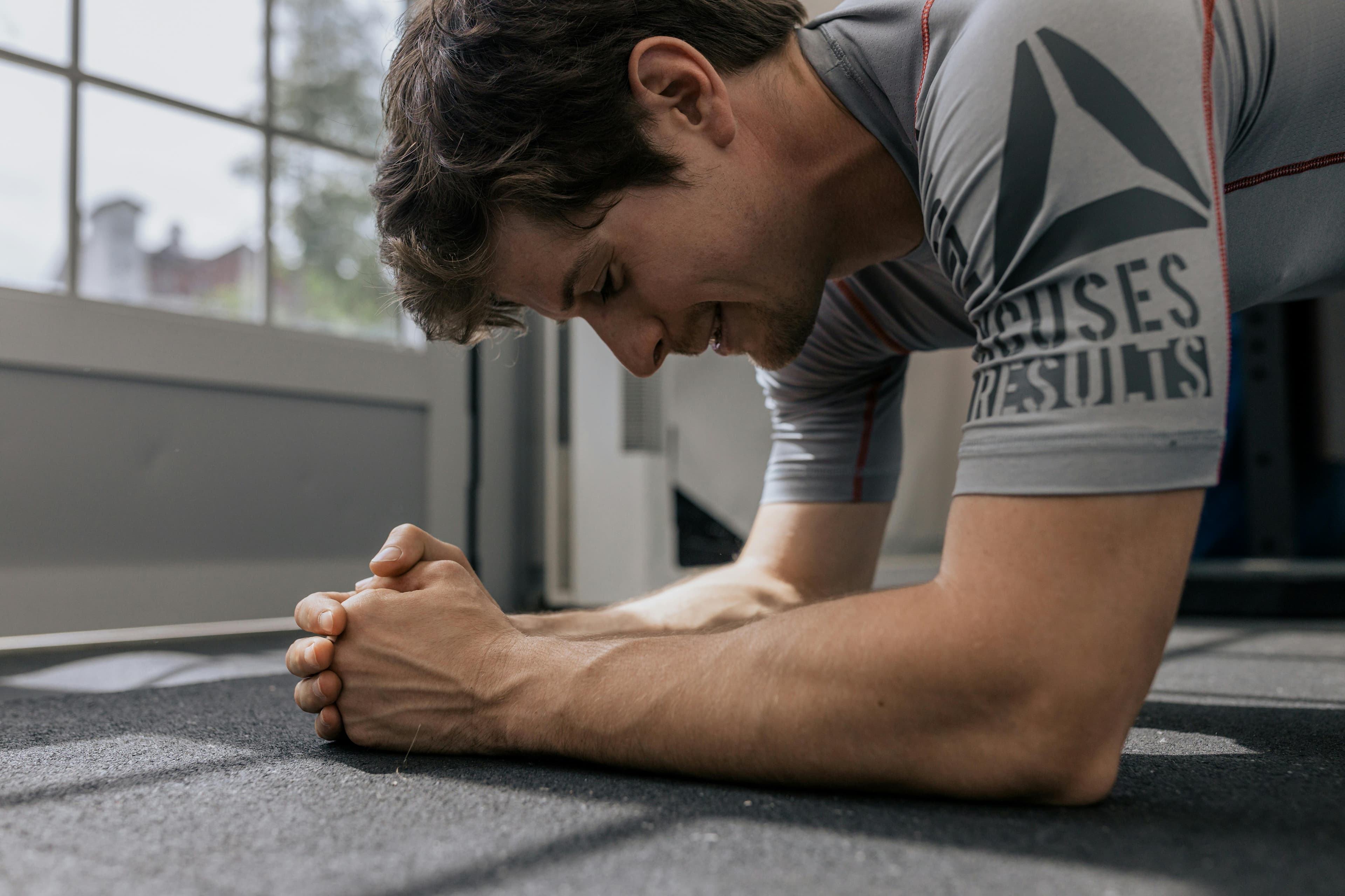 Focused man doing a plank exercise inside a gym for a core workout.