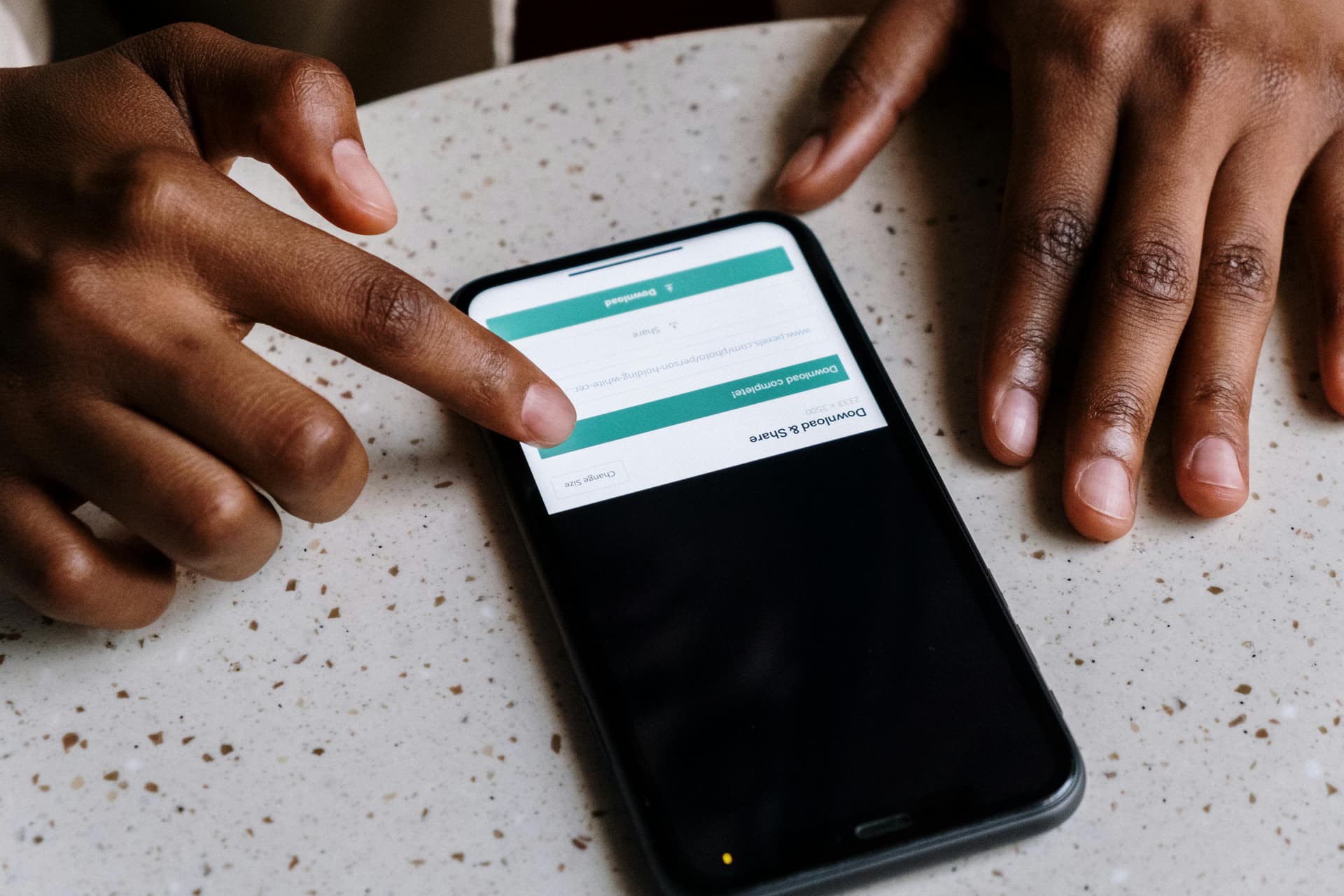 Close-up of hands interacting with a smartphone, displaying downloading interface.