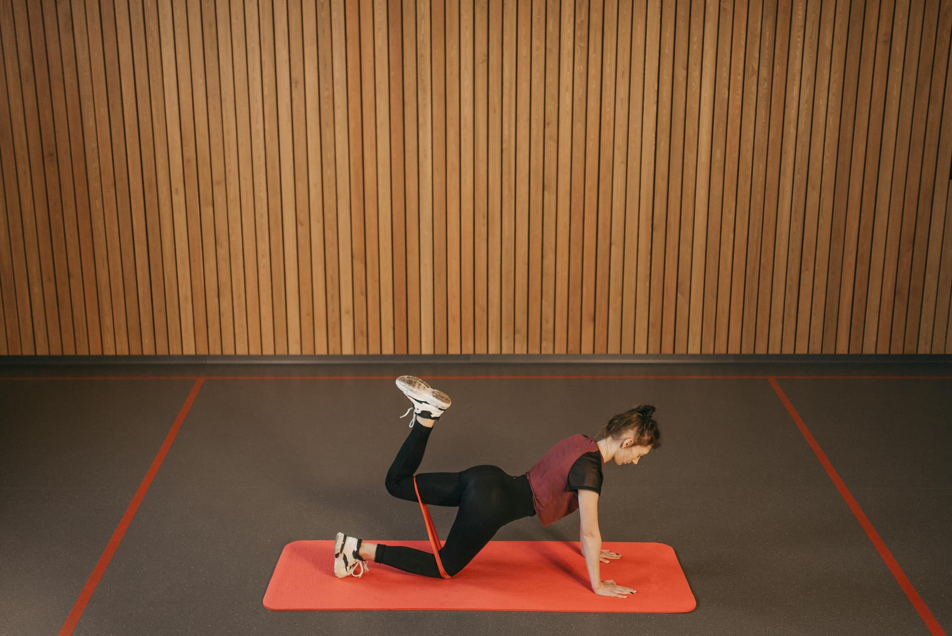 Woman performing a resistance band workout on a mat indoors, focusing on fitness and strength.