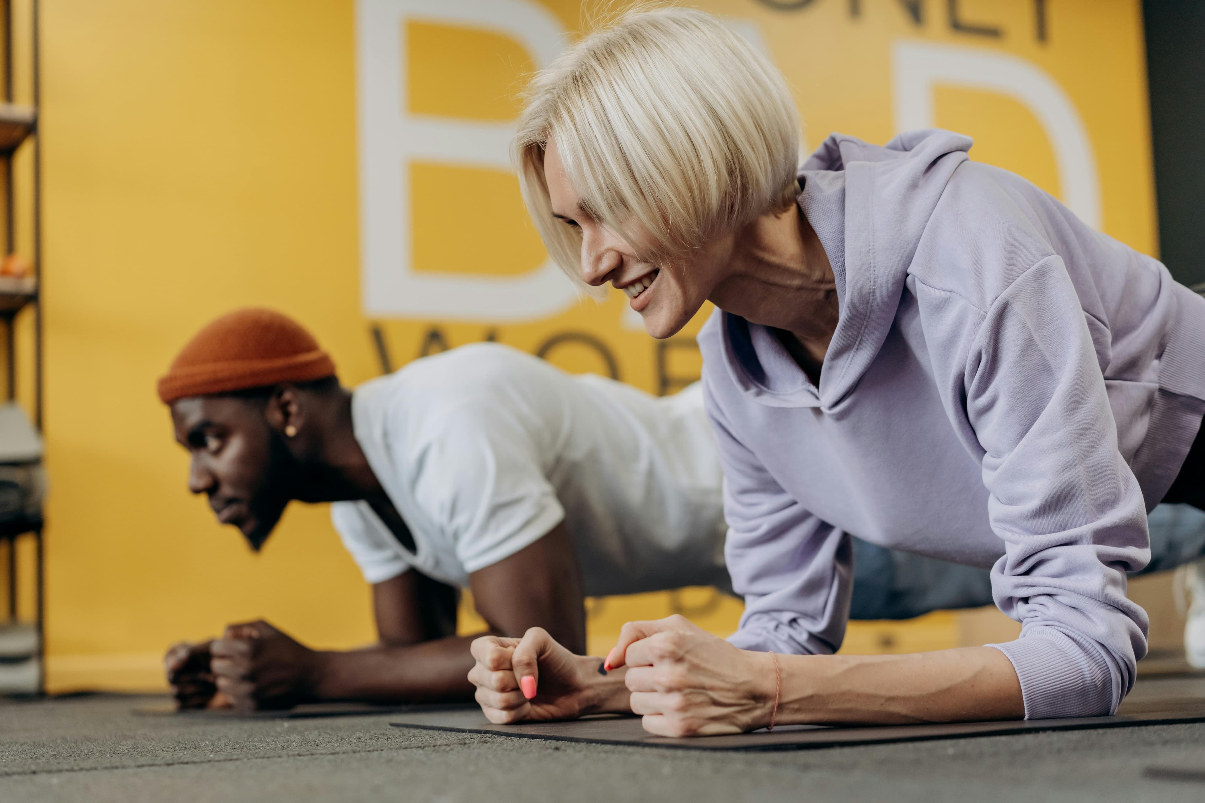 Two adults in sportswear doing plank exercises in a gym, focusing on strength and fitness.