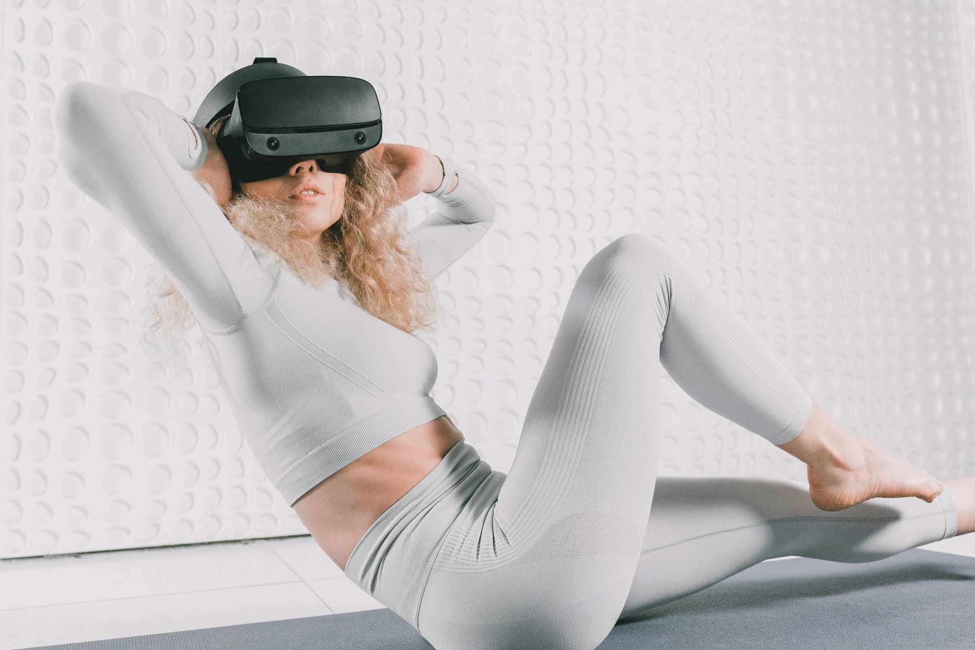 Female in workout attire using a VR headset while exercising indoors.