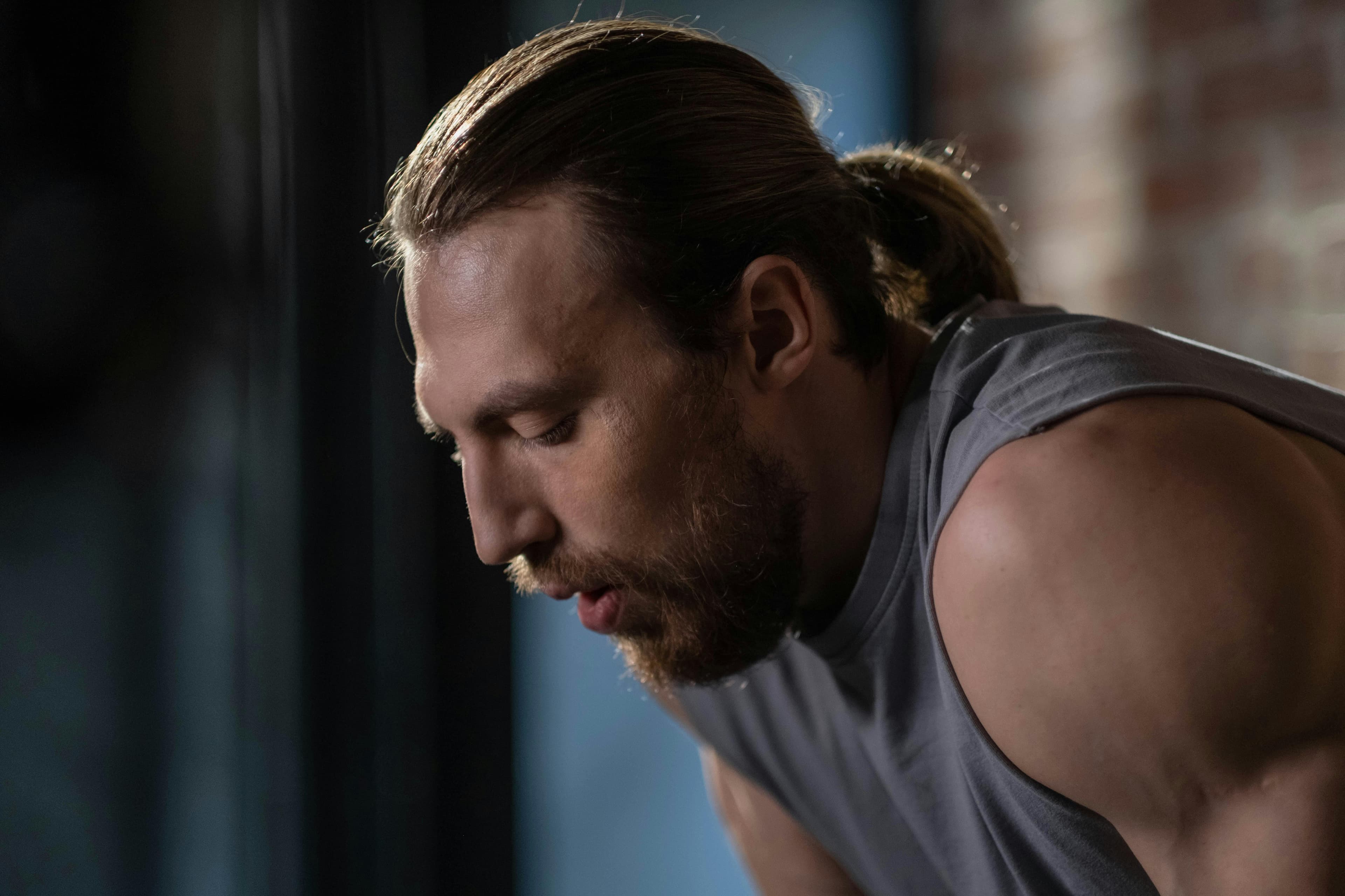 Close-up of a muscular man resting indoors, capturing a thoughtful moment post-exercise.