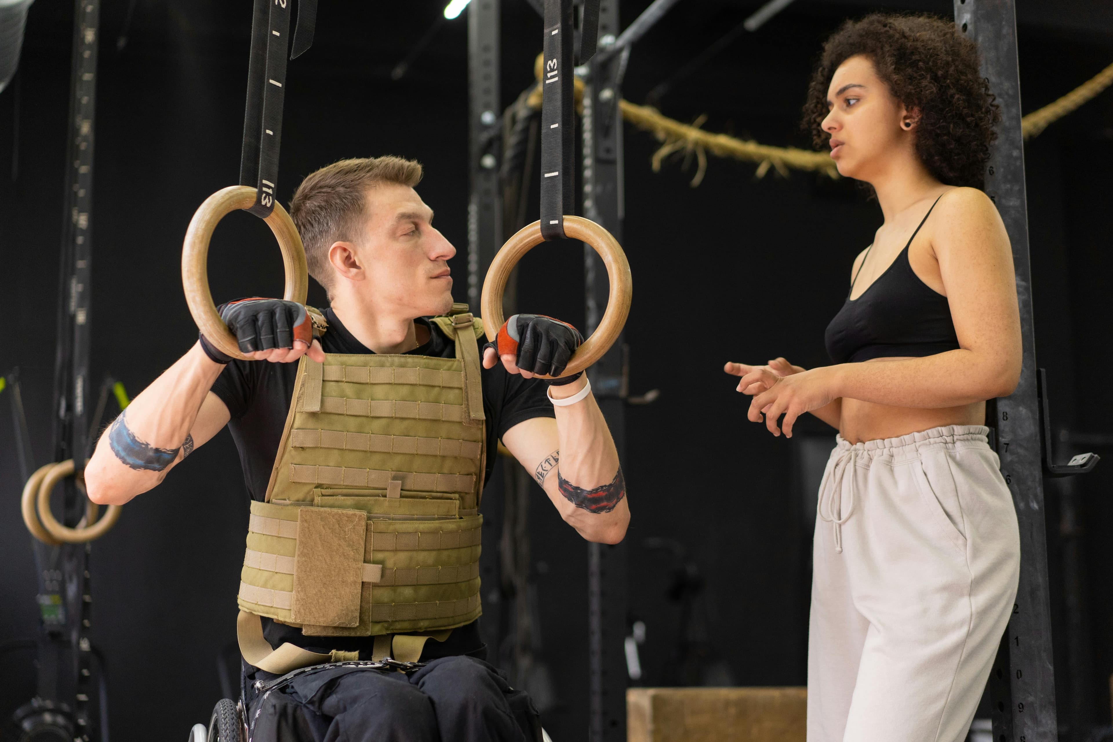 Adaptive athlete engaged in fitness training with personal trainer on gymnastics rings in a gym setting.