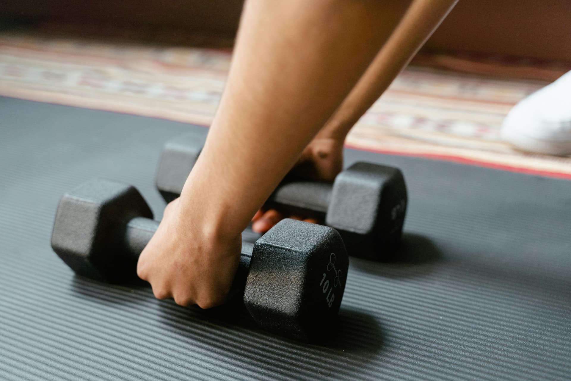 Close-up of a person picking up dumbbells on a yoga mat, emphasizing fitness and exercise.