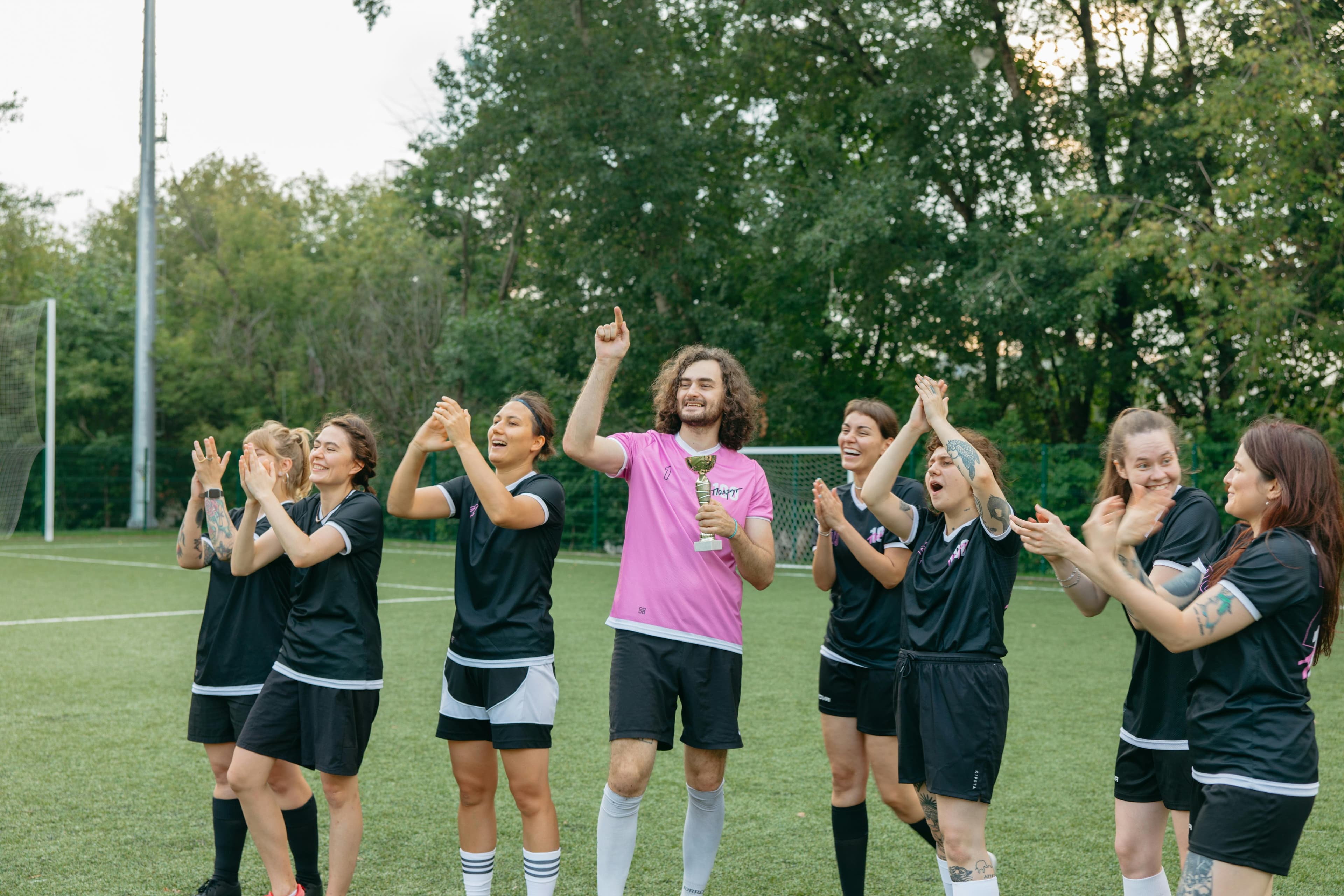 Joyful soccer team celebrating victory on outdoor field with trophy.