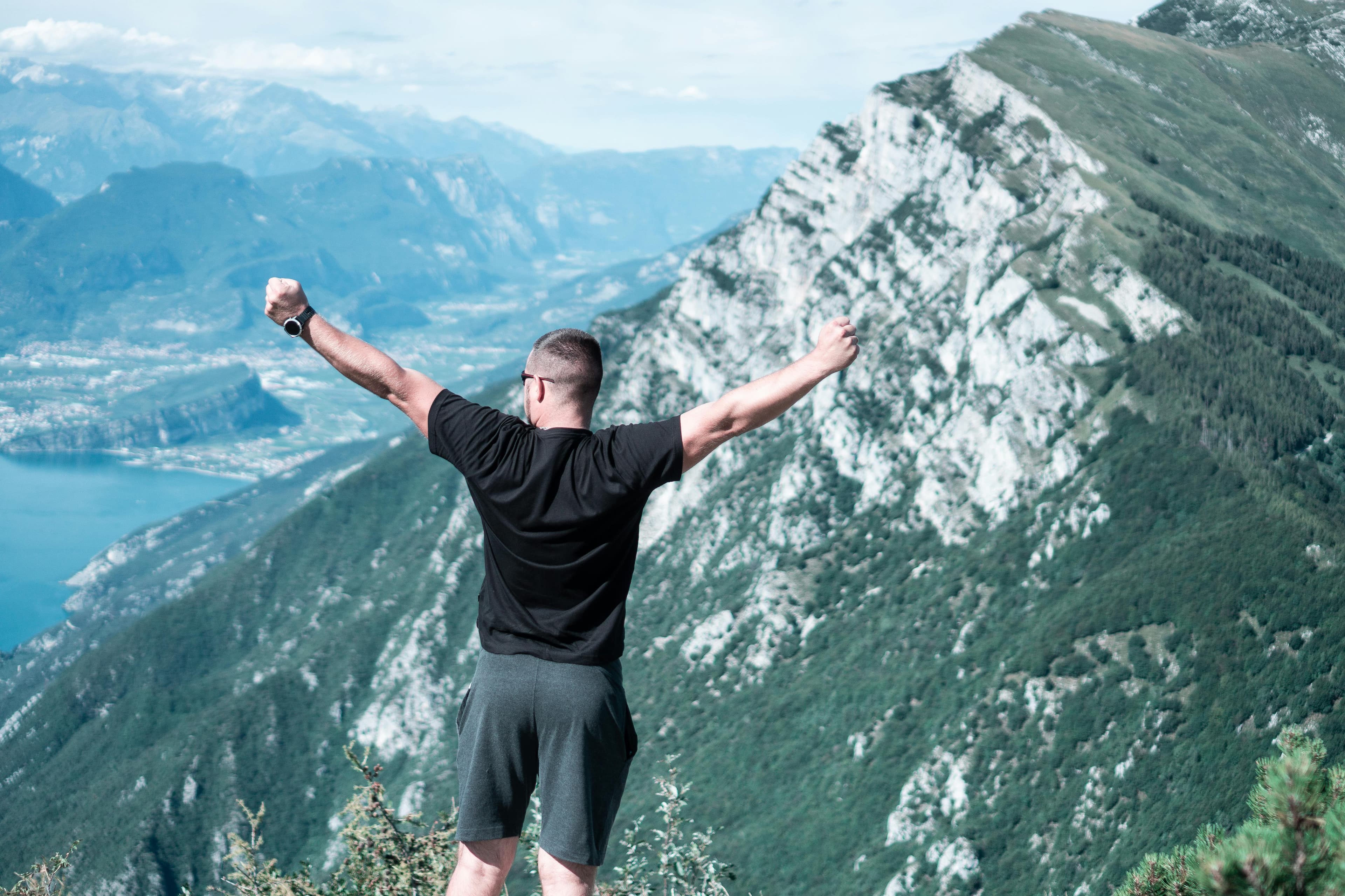 Man standing with arms raised in celebration overlooking a breathtaking mountain landscape.